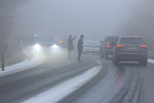 제주도 산간에 대설주의보가 내려진 30일 오전 516도로 성판악 부근에서 미끄러짐 사고가 발생하자 차에서 내린 운전자들이 수신호로 차량 흐름을 유도하고 있다.연합뉴스